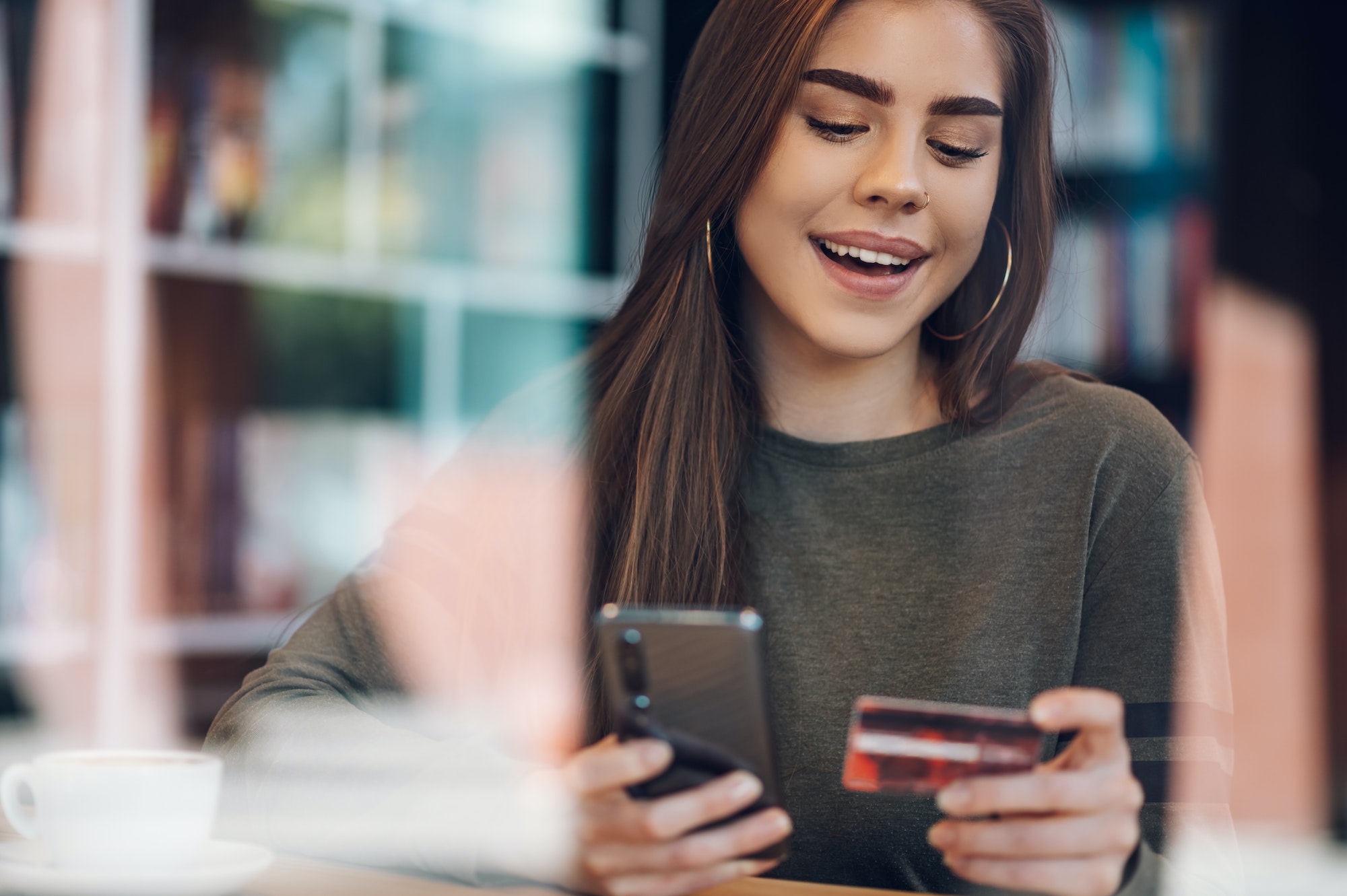 Woman using smartphone and a credit card for online shopping in a cafe